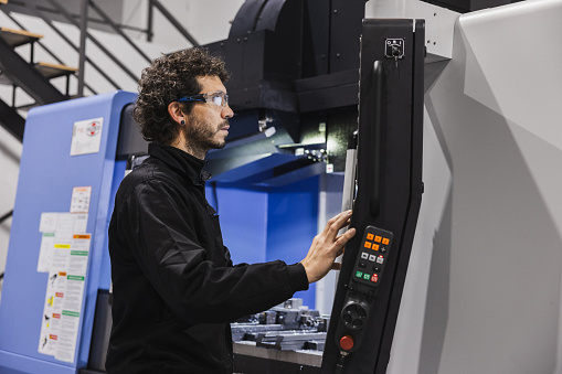 A focused view of a complex control panel of metalworking CNC milling machine, with an engineer meticulously working on machinery. Industrial work concept.