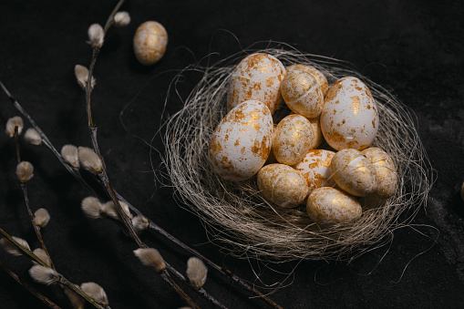 golden and white eggs in the nest beside the wilow on black rustic background. easter background. High quality photo