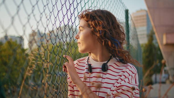 lonely girl posing sunlight chewing gum close up. teenager leaning on fence net - chewing gum audio zdjęcia i obrazy z banku zdjęć