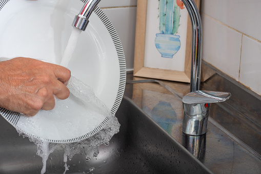 Hands washing a dish under the faucet.