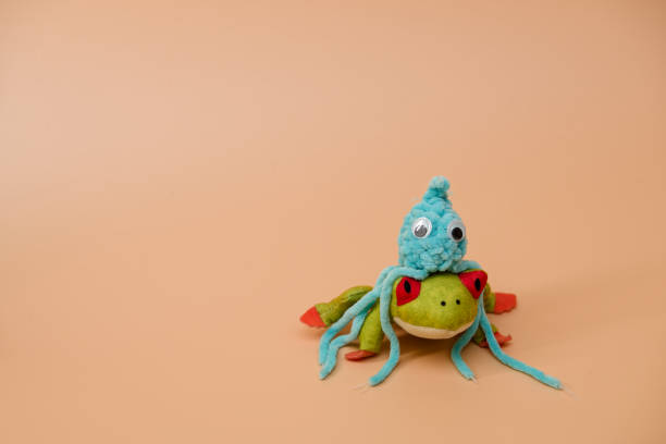 Crochet blue octopus toy sitting on a plush frog, orange background, advertising or presentation concept
