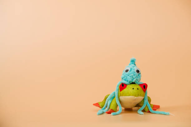 Crochet blue octopus toy sitting on a plush frog, orange background, advertising or presentation concept