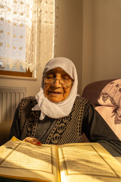 Muslim old woman reciting the Quran in the golden hour An elderly Muslim woman with pious glasses reads the Quran on her gold watch in her home diyarbakırda bayan eskort stock pictures, royalty-free photos & images