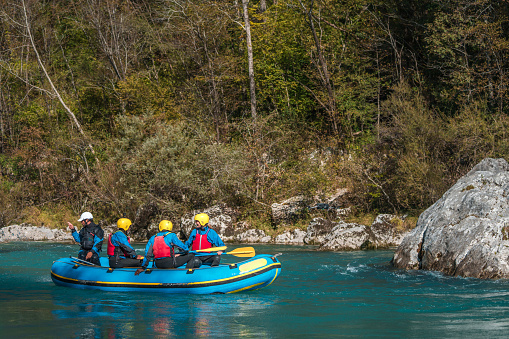 Seniors of diverse backgrounds share an adventure, paddling in unison on a peaceful river, clad in protective gear against a backdrop of vibrant autumn foliage.