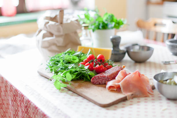 Kitchen table with ingredients for preparing pizza. Cooking process at home. Vegetables, cheese, greens, salami, tomatoes are on wooden boards.