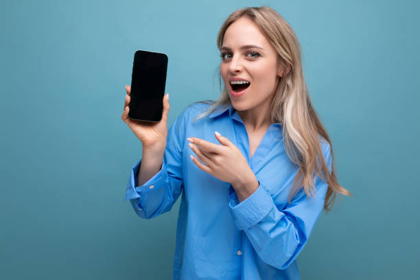 istock surprised blond girl holding a smartphone with a screen at the camera with an empty mockup for a website on a blue background 1956130166