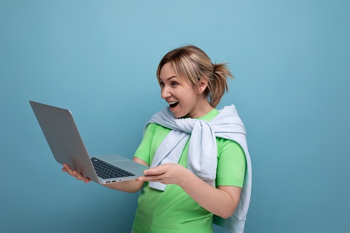 young surprised woman in casual outfit holding a laptop in her hands on a blue background.