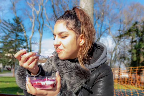 Beautiful teen girl sitting on bench in park and enjoying a sweet and delicious cake. Street foods are popular among tourists and people. Food concept.