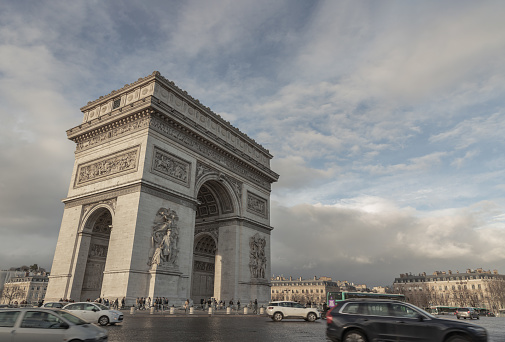 France, Paris - Jan 03, 2024 - Famous Arc de Triomphe (Triumphal Arch) at the city center of Paris and traffic trails in Chaps Elysees. Symbol of the glory and historical heritage, Iconic touristic architectural landmark, Tourism and travel concept, Space for text, Selective focus.