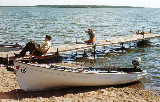 A man and a woman relax on a dock at a resort in the late 1940s.