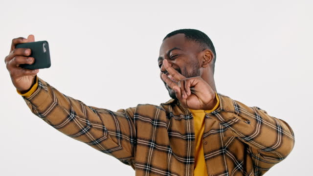 Online, black man or influencer taking a selfie in studio on social media with peace sign. Fashion, smile or cool happy African person taking a photo, vlog or picture isolated on white background