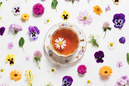 Herbal tea in a vintage porcelain mug with spring and summer flowers on white background. Flat lay, bright colorful pattern, top view. Summer country creative concept