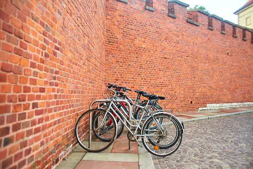 Bicycles are parked in a special parking lot near the large wall of the castle made of old red brick in the old streets of Europe in the center of Krakow