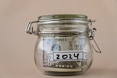 Saving Money In Glass Jar filled with Dollars banknotes. 2024 year transcription in front of jar. Managing personal finances extra income for future insecurity