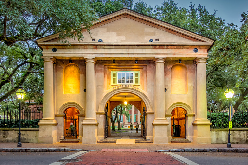 People walk on the historic College of Charleston campus in Charleston, South Carolina, USA in the evening, as seen through the Gatehouse at Randolph Hall.