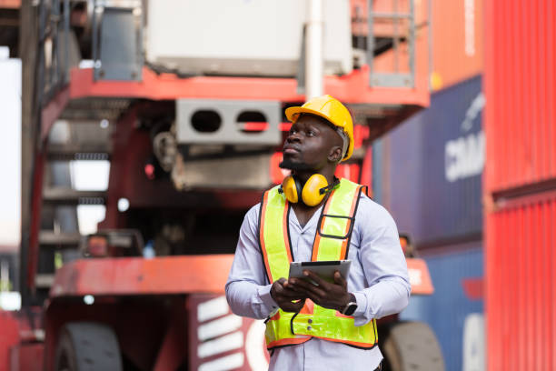 istock African American male container yard worker working and checking container boxes before loading at commercial dock site. Black male people worker inspecting container boxes from cargo freight ship 1956575602