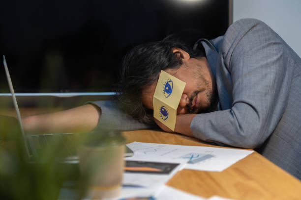 istock Tired sleepy businessman with stickers, adhesive notes on eyes sleeping at workplace, sitting at work desk in office 1956708374
