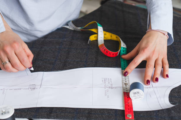 Dressmaker marks piece of fabric with chalk according to paper pattern. Work of tailor, tools for sewing