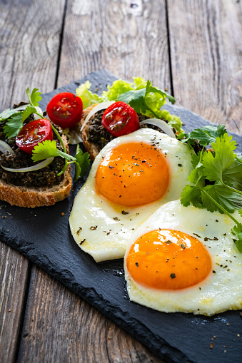 Breakfast - sunny side up egg, tapenade bruschetta and fresh vegetables on wooden table