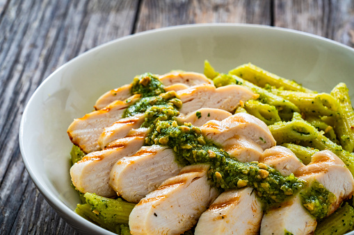 Grilled chicken breast and penne noodles with basil pesto sauce on wooden background