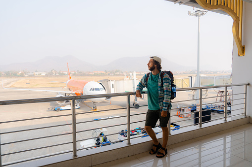 Man with backpack walking in the terminal of an airport on the background of the plane