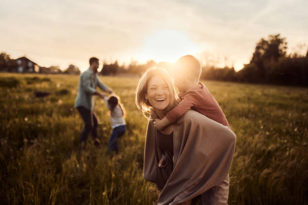 istock Cheerful mother piggybacking her son in nature at sunset. 1956802492