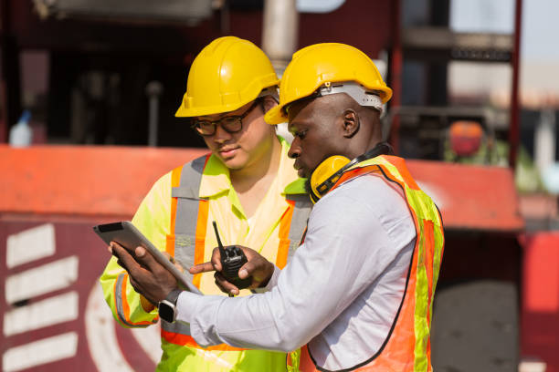 istock Group of diverse male container yard worker working and checking container boxes at commercial dock site. Black male and Asian male people worker inspecting container boxes from cargo freight ship 1956828128