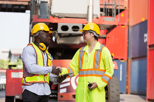 Group of diverse male container yard worker working and checking container boxes at commercial dock site. Black male and Asian male people worker inspecting container boxes from cargo freight ship