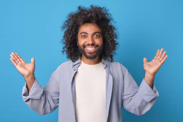 istock Young cheerful smiling Arabian man raises hands up stands in studio 1956867399