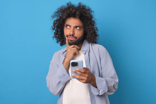 istock Young thoughtful attractive Arabian man with phone in hands stands in studio 1956870489