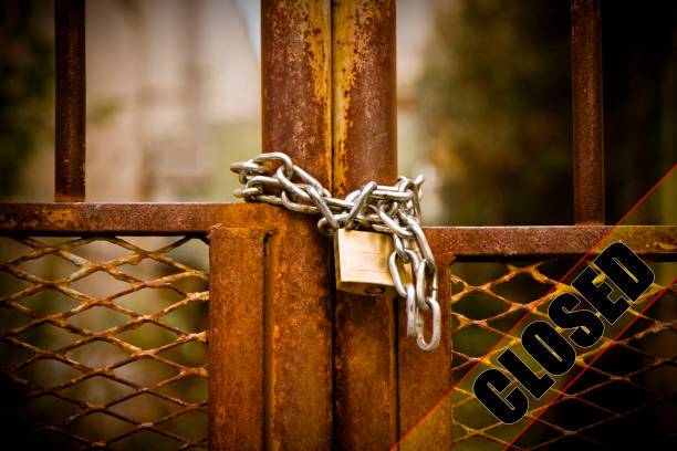 istock Rusty metal gate of a factory closed with padlock - concept image with closed text on it 1956876450