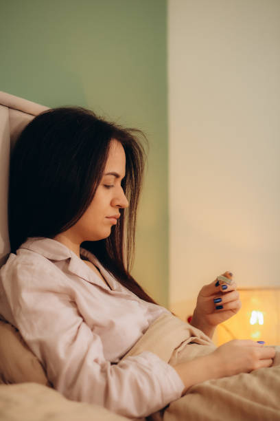 istock Sick woman measuring checking body temperature looking at thermometer while lying on bed at home 1956884490