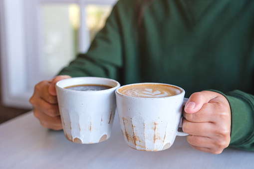 Closeup image of a woman holding and clinking two cups of hot coffee