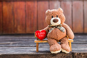Brown teddy bear with I love you red heart on wooden bench with space on blurred wood background