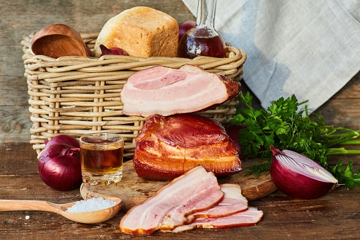 The meat bacon lies on a wooden table surrounded by vegetables and other products. Meat production