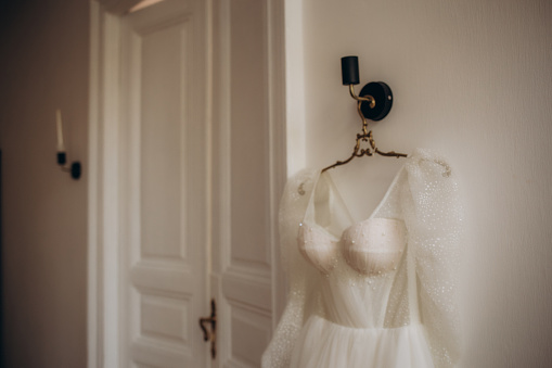 Elegant wedding dress hanging on rack indoors. High quality photo
