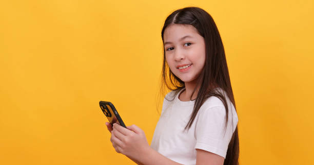 istock Cute little girl using smart phone on a yellow background. 1956929697