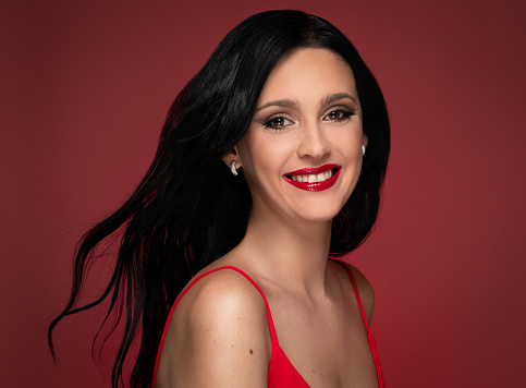 Beauty studio portrait of young beautiful smiling woman against red background