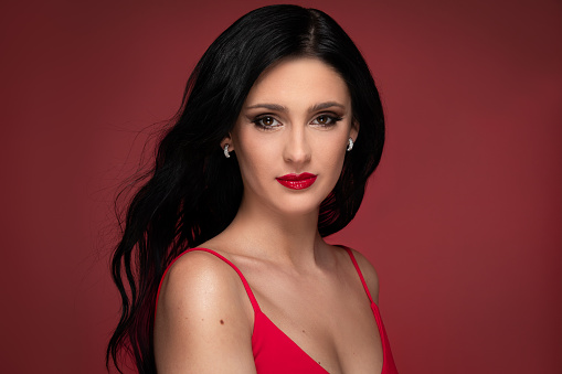Beauty studio portrait of young beautiful confident woman against red background