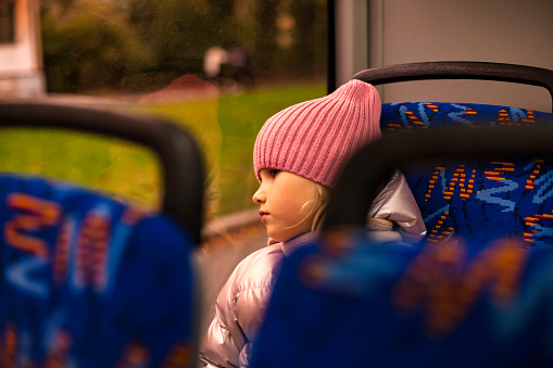 Child girl 5 year old travels on metropolitan bus public transport, looking at window. Kid girl in casual wear riders in trolleybus, city lifestyle. Public urban transport concept. Copy ad text space