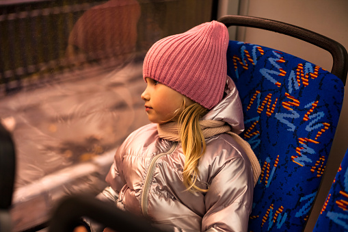 Child girl 5 year old riders on metropolitan bus public transport, looking at window. Kid girl in autumn wear travels in trolleybus, city lifestyle. Public urban transport concept. Copy ad text space