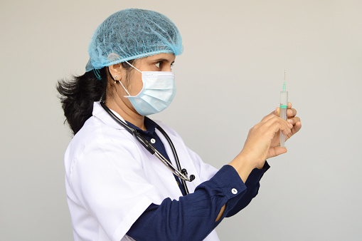 Horizontal photo of one woman nurse or doctor or health care worker, physician getting ready with a syringe in her hand to administer an injection dose over gray background with copy space for text.