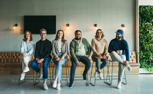 Portrait of a happy group of business colleagues seated together in a row within their office environment. Business men and women showing unity and a shared purpose of achieving success.