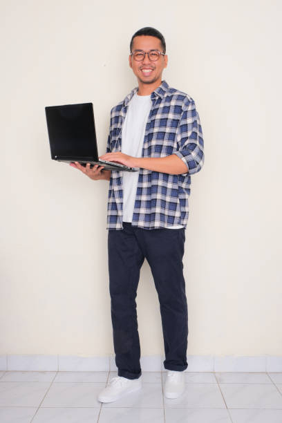 istock Full body portrait of a man smiling at the camera while using a laptop 1956990651