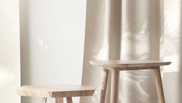 istock Two wooden geometric shape brown chairs with different height in sunlight, leaf shadow on beige curtain, wall 1956993371