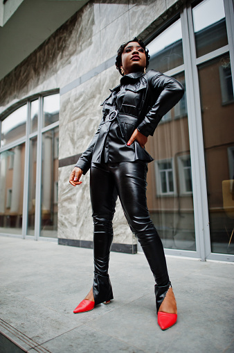 Fashionable beautiful african american woman posing in black leather jacket and pants at street.