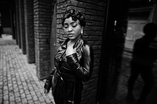 Fashionable beautiful african american woman posing in black leather jacket at street.