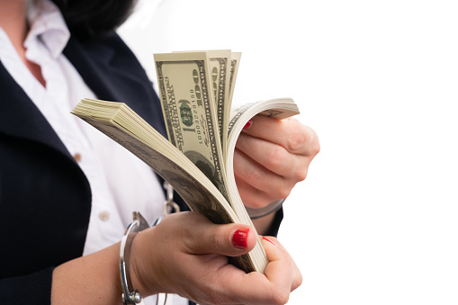 Close-up of illegal cash money counted by adult businesswoman in handcuffs as corruption punishment concept isolated on white background
