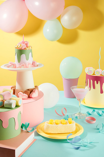 Origami birthday cakes decorated with colorful marshmallows. A cake, a pink cocktail, balloons and decorative ribbons. Lively birthday background.