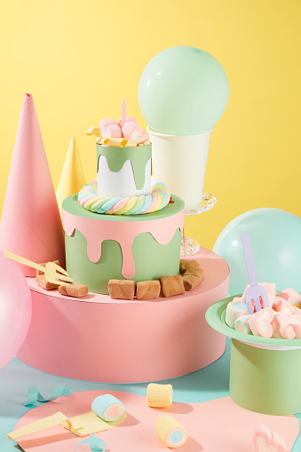 Close-up of a three-tier origami cake decorated with marshmallows. Balloons and birthday hats are decorated around the background. Creative space.